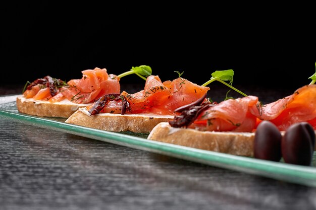 Bruschetta con trucha, salmón, queso crema y microgreen sobre una placa de vidrio