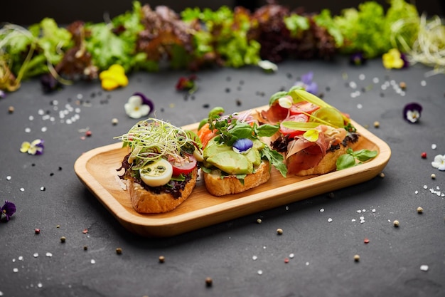 Bruschetta variada con parma de salmón y fuente de pesto Bocadillos antipasti italianos Mezcla variada de sándwiches pequeños sobre fondo oscuro Foto para el menú del restaurante