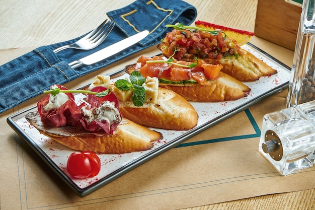 Bruschetta variado sortido em um prato branco. Baguete branca com jamon, torrada com molho de tomate, brusqueta com salmão e queijo azul. Configuração de mesa de restaurante. Fechar-se