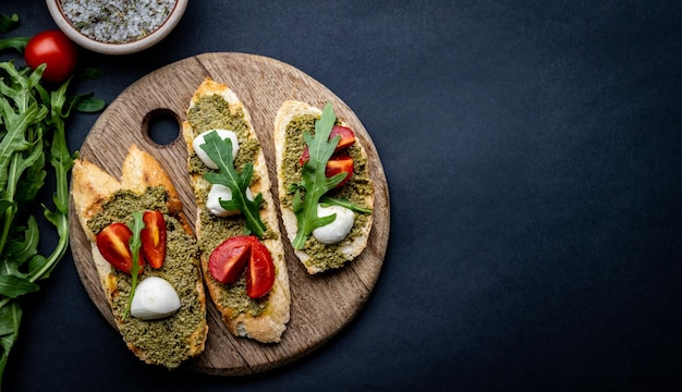 Bruschettas com queijo mussarela de tomate pesto e manjericão na placa de madeira com pão torrado italiano