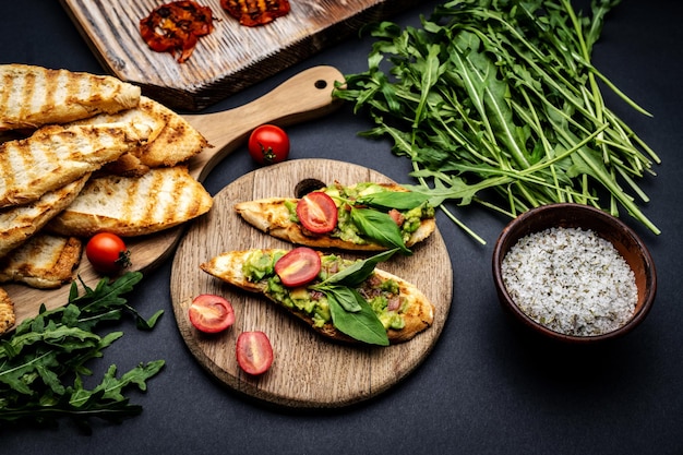 Bruschettas com torradas guacamole manjericão e tomate cereja na tábua de madeira servido com rúcula mexic