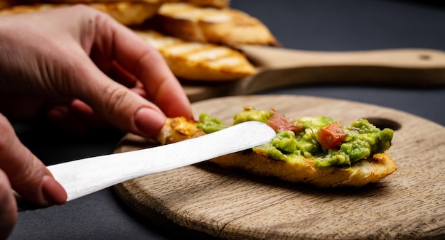 Bruschettas con tostadas de guacamole y tomates cherry en tablero de madera manos de persona preparar con cuchillo