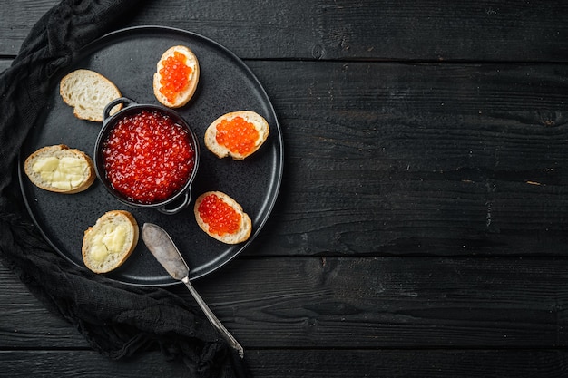 Bruschettes con caviar rojo de mantequilla, sobre mesa de madera negra, vista superior plana con espacio de copia