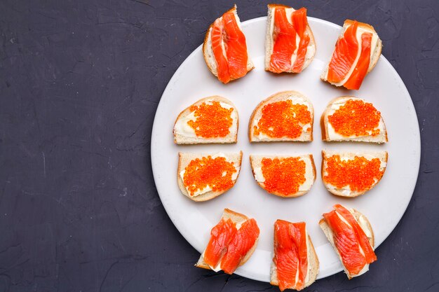 Bruschettes mit Butter und rotem Kaviar und Lachs auf einem weißen Teller auf einem grauen Betonhintergrundkopierraum. Horizontales Foto