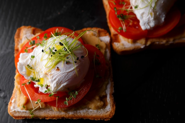 Bruschettes mit Kaviar, Tomate und pochiertem Ei, auf einem schwarzen Stein und einem Holzbrett, Draufsicht