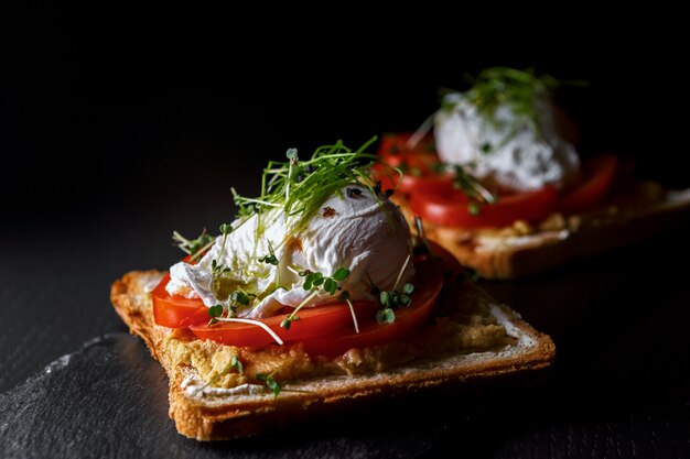 Bruschettes mit Kaviar, Tomate und pochiertem Ei, auf schwarzem Stein und Holzbrett, Seitenansicht