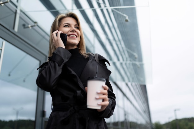 Brustbild einer blonden Geschäftsfrau mittleren Alters mit Handy und einer Tasse Kaffee