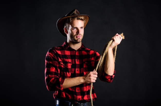 Brutal e confiante. Vida ocidental. Fundo preto de vaqueiro com barba por fazer do homem. Homem usando chapéu segurar corda. Ferramenta de laço de cowboy americano. Lasso usou eventos competitivos de rodeio. O laço pode ser amarrado ou enrolado.