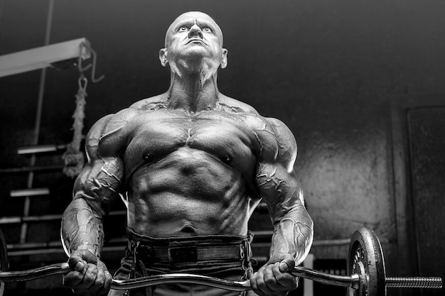 Brutal y musculoso fuerte culturista atlético hombre bombeando músculos en el entrenamiento en el gimnasio