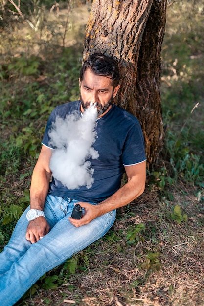 Brutaler Dampfer, der auf dem Waldboden ein elektronisches Rauchgerät raucht Vaping-Aktivität