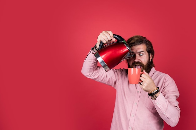 Brutaler kaukasischer Hipster mit Bart im Hemd hält Wasserkocher Haushaltsgeräte