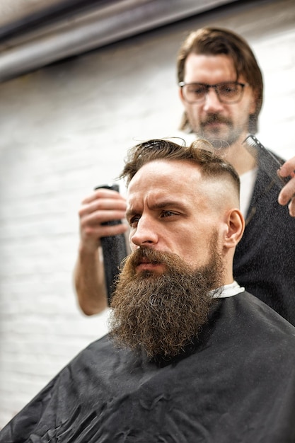 Brutaler Kerl im modernen Barber Shop Friseur macht Frisur ein Mann mit Bart Porträt des stilvollen Mannes Bart Friseurmeister macht Frisur und Stil mit Schere und Kamm