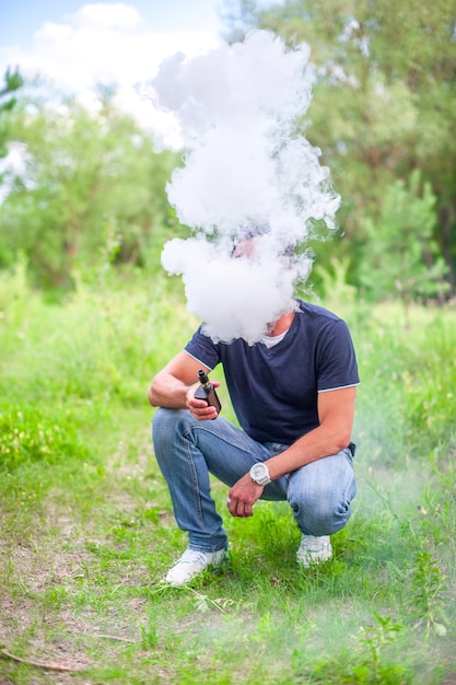 Brutaler Mann, der eine elektronische Zigarette auf dem Gras verdampft