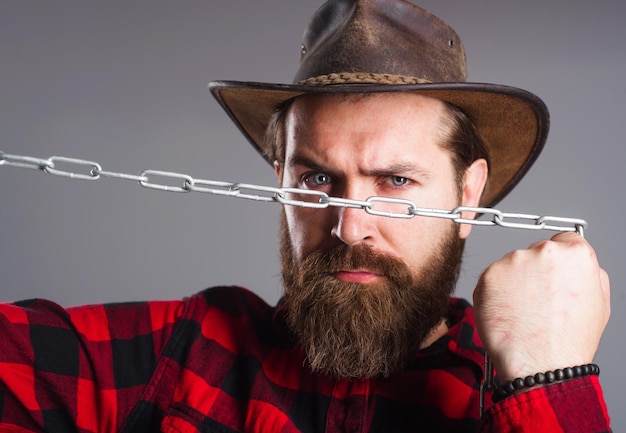 Brutaler Mann in Cowboyhut mit Kette Ernster bärtiger Mann in kariertem Hemd, der versucht, Metallketten zu brechen