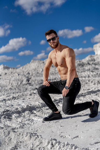 Brutaler starker Bodybuilder, der im Freien aufwirft. Fotoshooting im Steinbruch. Outdoor-Sportkonzept. Posieren und Muskeln pumpen. Weiße Landschaft.