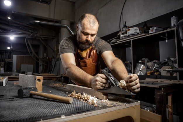 Brutaler Tischlermeister in einer Schürze Platanen mit einem Hobel in der Werkstatt