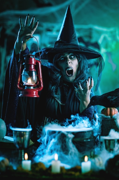 Bruxa com rosto horrível e lanterna na mão em um ambiente nebuloso assustador envia o mal. Conceito de dia das bruxas.
