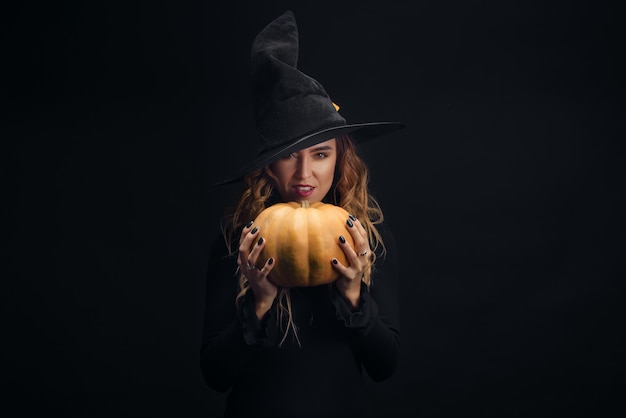 Uma Jovem Bruxa Bonita Em Um Chapéu Cônico Segura Uma Abóbora De Halloween  Em Suas Mãos E Faz Um Feitiço Com Sua Mão. Foto Royalty Free, Gravuras,  Imagens e Banco de fotografias.