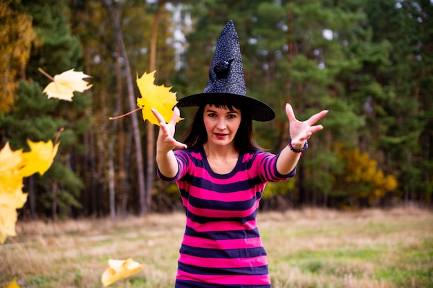 Bruxa joga folhas na floresta de outono. Mulher mágica festa fantasia de Halloween