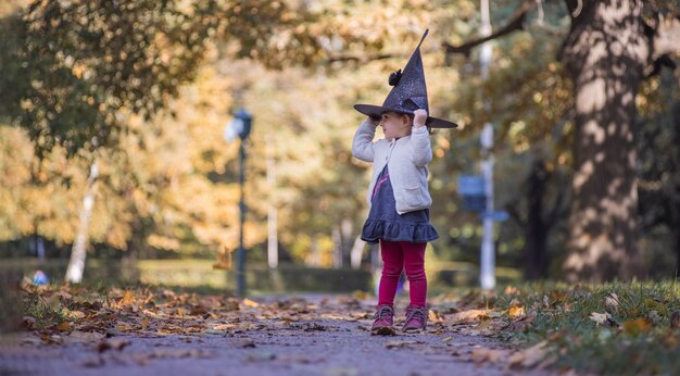 Bruxinha fofa com um chapéu em um parque de outono em um dia ensolarado de halloween