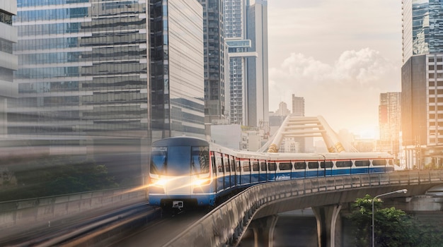 BTS Skytrain, tren eléctrico, corriendo en el camino con edificios de oficinas comerciales en el fondo.