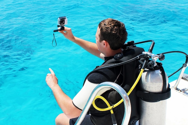 Buceador feliz con equipo y cámara se está preparando para su lección de buceo en el mar azul