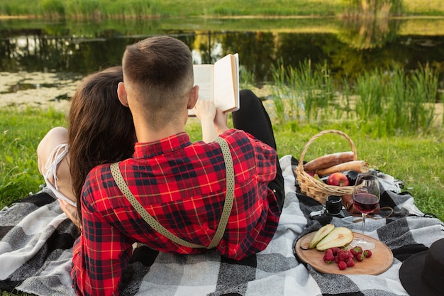 Buch lesen. Kaukasisches junges Paar, das am Sommertag zusammen ein Wochenende im Park genießt?