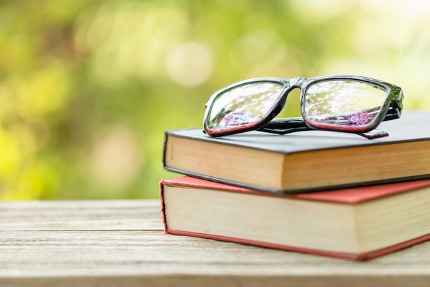 Buch und Brille auf Holztisch mit abstrakter grüner Natur verschwimmen Lese- und Bildungskonzept