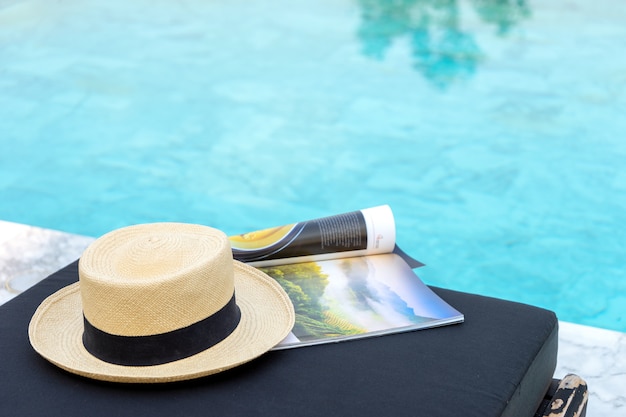 Buch und Hut auf der Sonnenliege am Pool,