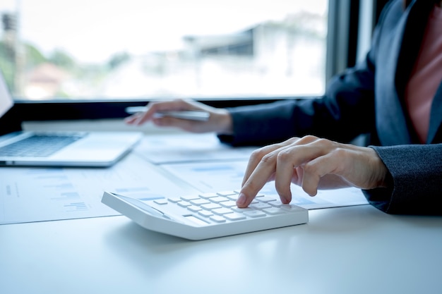 Buchhalter der Geschäftsfrauen verwenden Taschenrechner und Laptop, die Konto für die Zahlung der Steuer auf dem weißen Schreibtisch im Arbeitsbüro tun.