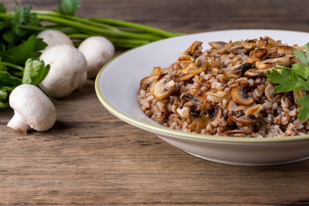 Buchweizenbrei mit Pilzen in einem weißen Teller auf Holzhintergrund