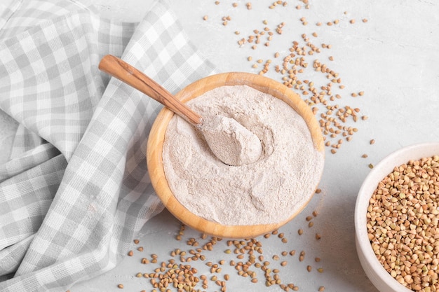 Buchweizenmehl in einer Holzschüssel mit Holzlöffel und rohem grünem Buchweizenkorn auf grauem Stein