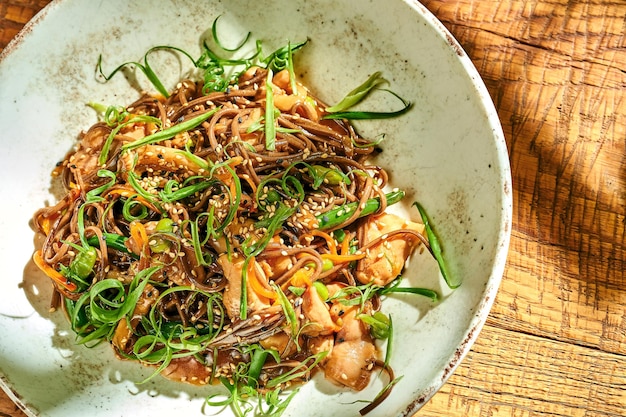 Buchweizennudeln Wok in Teriyaki-Sauce mit Hähnchen in einem Teller auf Holzhintergrund