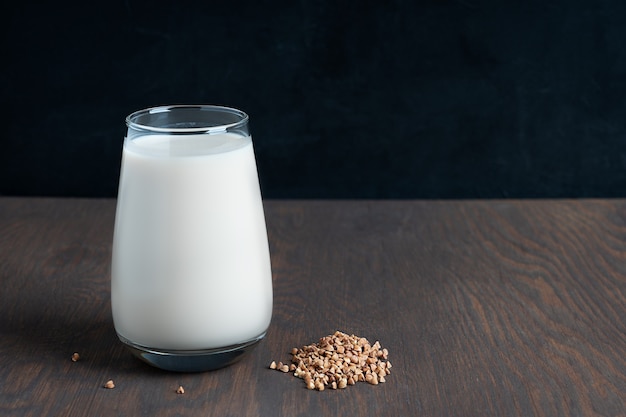 Buchweizensamen und Glas laktosefreie Milch auf dunklem Holztisch