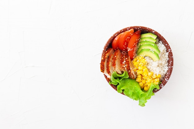 Buda tazón con arroz, tomate, maíz, pollo y aguacate sobre una mesa blanca