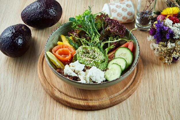 Buda tazón con pepinos, tomates, guacamole y salmón, queso feta y lechuga en una mesa de madera. Comida sana y equilibrada. Nutrición fitness. Vista superior, comida plana.