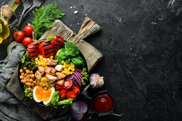 Buddha bowl frango grão de bico brócolis tomate ovo páprica cebola em um prato preto sobre um fundo preto vista superior espaço livre para o seu texto