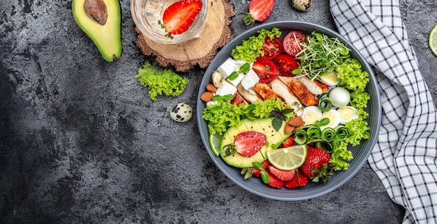 Buddha Bowl Gericht mit Hähnchenfilet, Avocado, Fetakäse, Wachteleiern, Erdbeeren, Nüssen und Salat. Detox und gesundes Superfoods-Schüsselkonzept. Langes Bannerformat. Ansicht von oben.