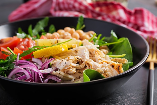 Buddha Bowl Gericht mit Hähnchenfilet, Kichererbsen, Tomaten, roten Zwiebeln, frischem grünem Salat und Samen-Sesam. Gesunde ausgewogene Ernährung.