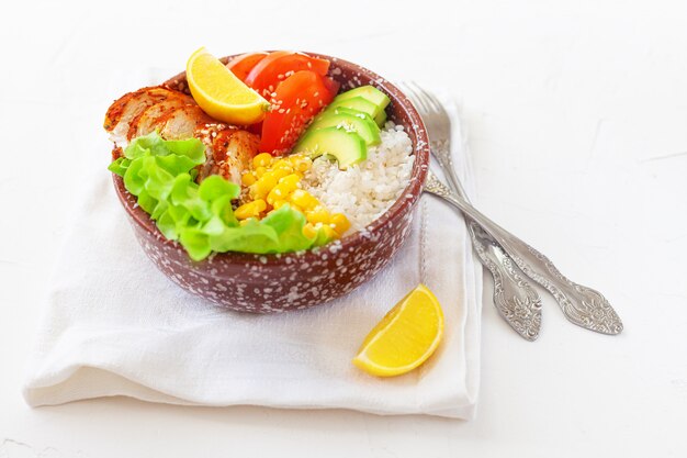 Buddha-Schüssel mit Reis, Tomaten, Mais, Huhn und Avocado auf einem weißen Tisch