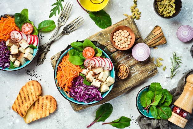 Buddhas vegane Schüssel Tofu-Käse Spinatkohl Radieschen und Karotten Das Konzept der gesunden Ernährung Auf einem Steinhintergrund Ansicht von oben