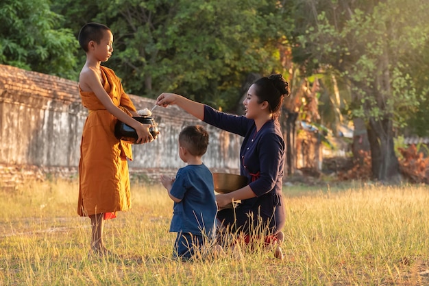 Buddhistischer älterer Anfänger. Die Familie Kinderfrau, die Speiseangebote in die Almosenschale eines Mönchs legt, und eine Frau, die sich niederwirft, um Anbetungsmönche zu respektieren, Mönche, die jeden Morgen Routine gehen.