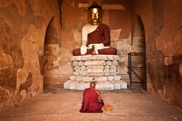 Buddhistischer Mönch sitzt und betet vor der Buddha-Statue in der antiken Stadt Bagan, Myanmar