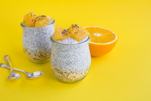 Budín con chía, copos de avena y naranja en los frascos de vidrio sobre fondo amarillo