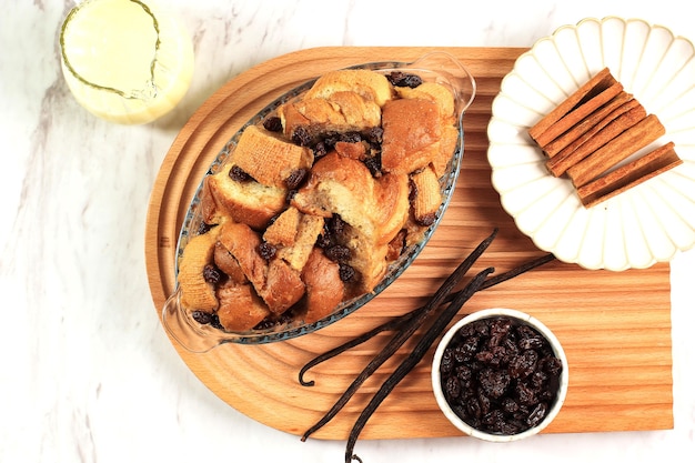 Budín de pan de vainilla y mantequilla con pasas en una fuente transparente para hornear, servido con Vla, vista superior