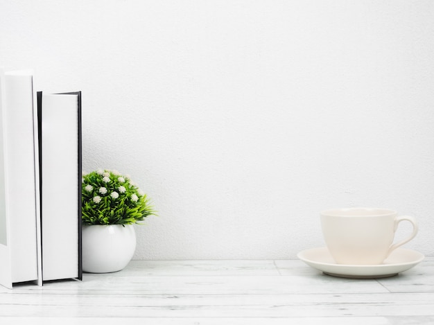 Bücher und kleine Vase auf weißem Holztisch im minimalistischen Stil Kopienraum weiße Wand, Arbeitsbereich zu Hause