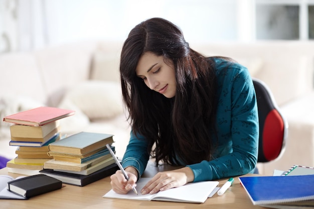 Bücherbildung und Mädchen schreiben in einem Buch für Lernaufgaben oder Hausaufgaben in ihrem Zuhause. Studentin und Notizbuch am Tisch für Projektplanung und Brainstorming, kreative Notizen und Ideen