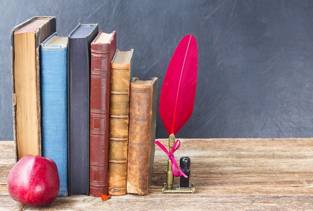 Bücherregal aus Holz mit alten Büchern, Apfel und rotem Federstift