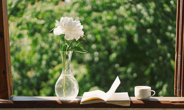 Büchertasse Kaffee und weiße Pfingstrosen auf einem Holzfenster. Romantisches Konzept im Vintage-Stil
