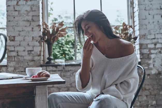 Buen día. Mujer joven atractiva manteniendo los ojos cerrados y comiendo frambuesas